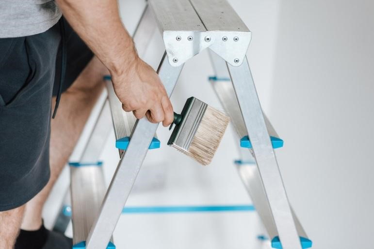 A man climbing a ladder with a paintbrush in hand