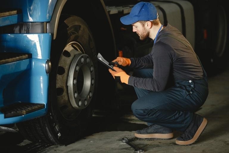 A man squatting next to the front tire of an 18-wheeler truck